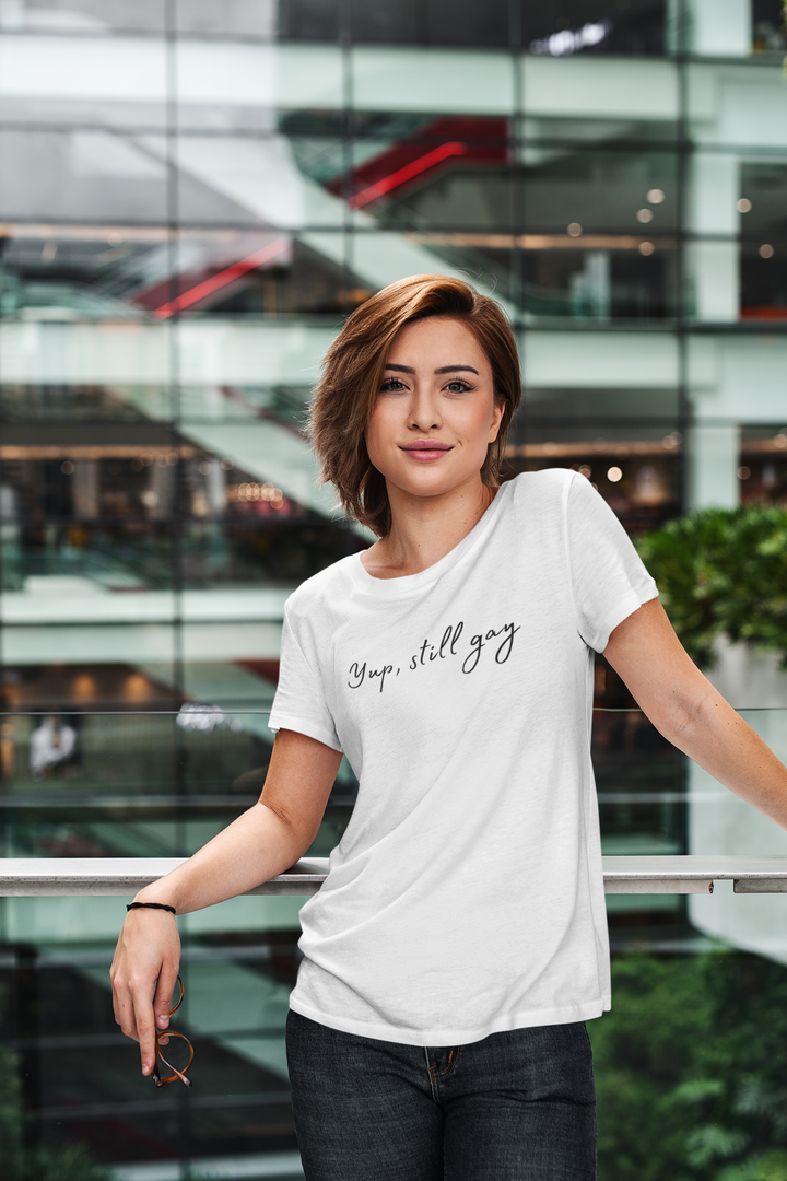 Woman with short hair wears a white t-shirt that reads "Yup, still gay"